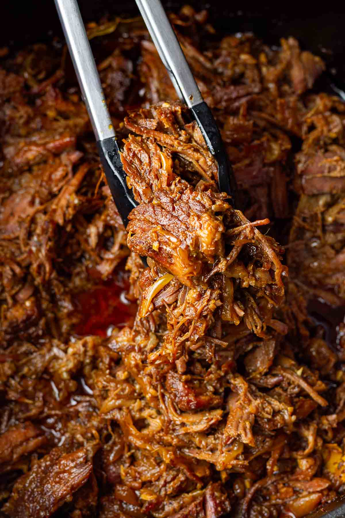 picking shredded beef from the pot with tongs
