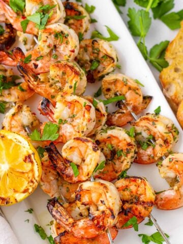marinated grilled shrimp skewers stacked on a plate with charred lemon