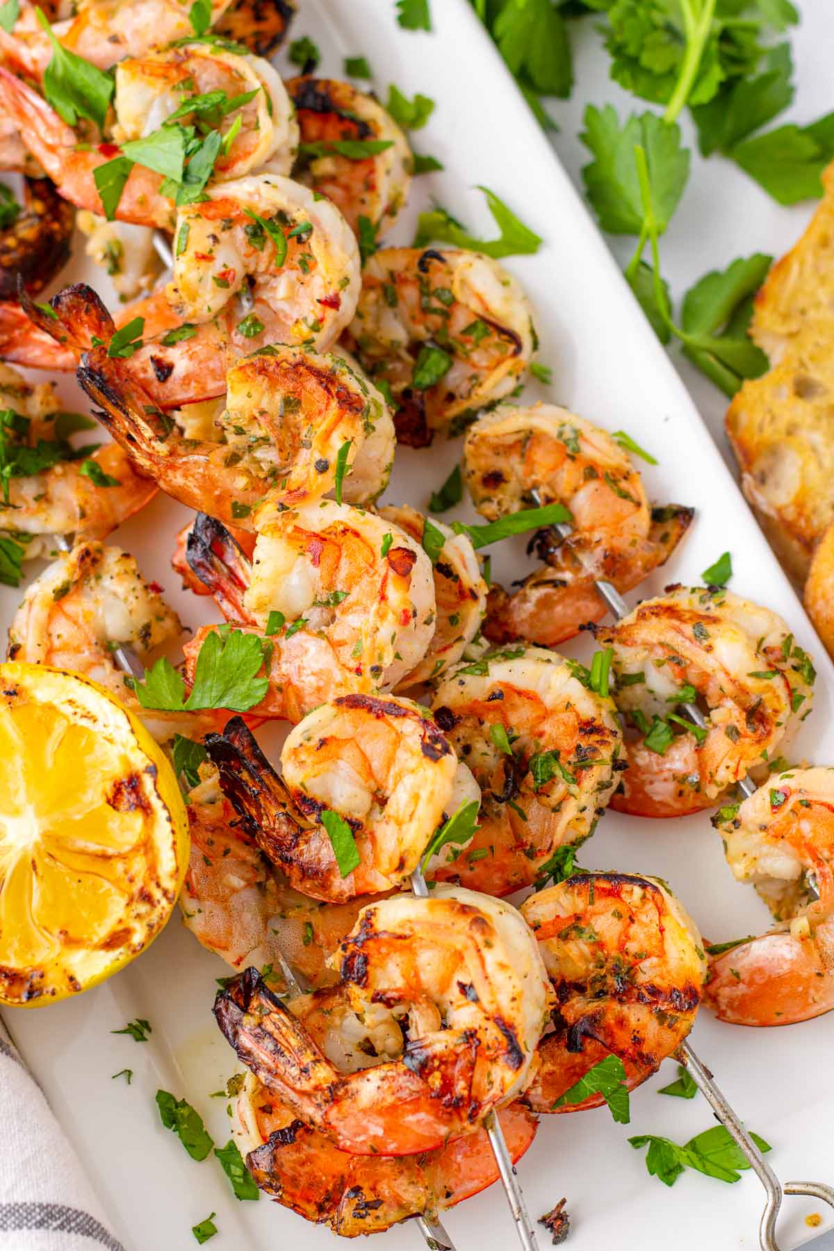 marinated grilled shrimp skewers stacked on a plate with charred lemon