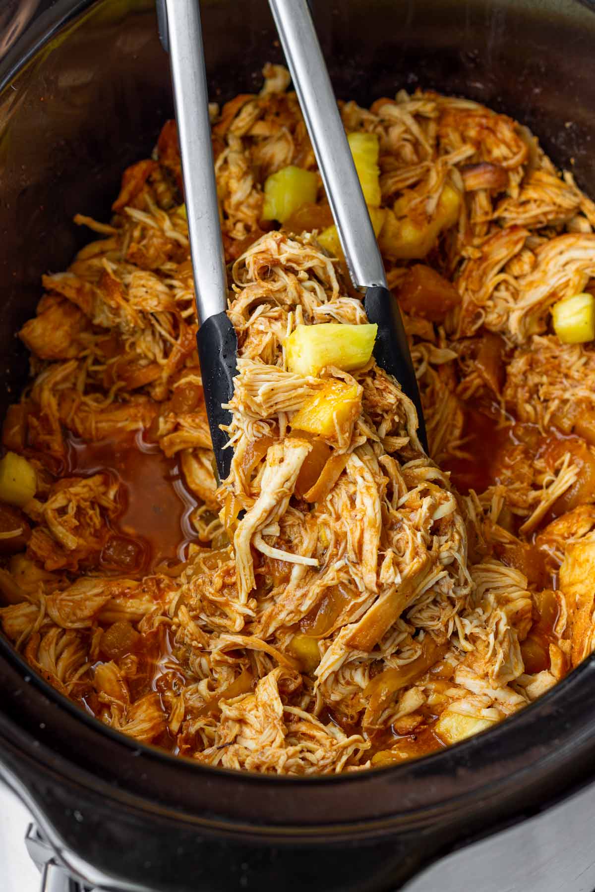 picking up pulled chicken with pineapple using tongs
