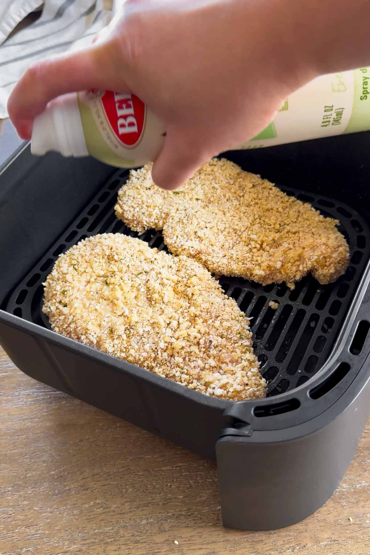 spraying breaded chicken cutlets on the air fryer basket