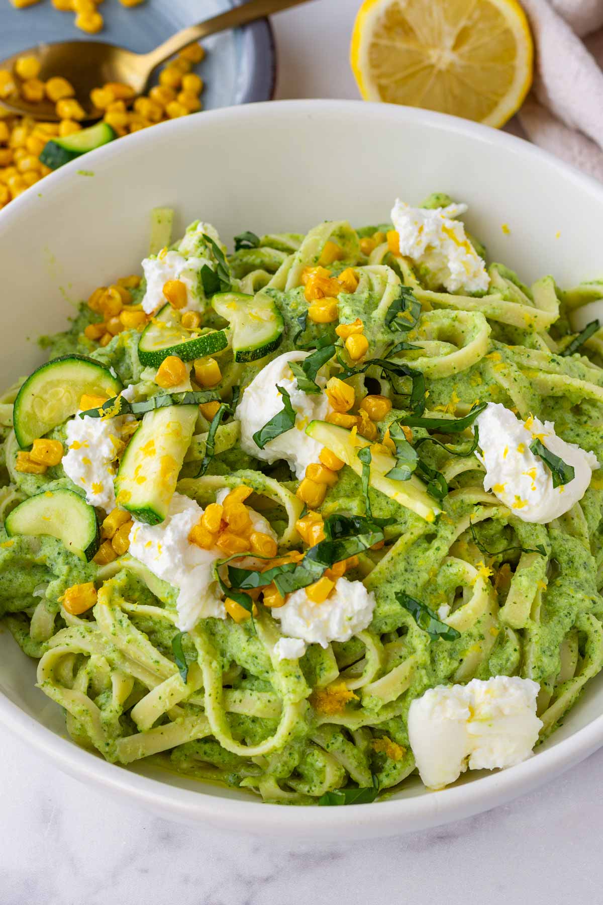 bowl of creamy zucchini pasta topped with corn, basil, burrata, sauteed zucchini