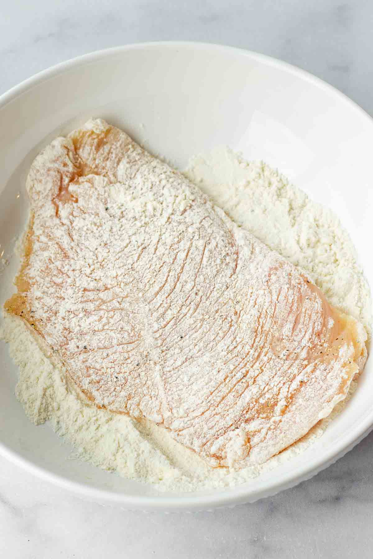 flouring chicken cutlet in a bowl