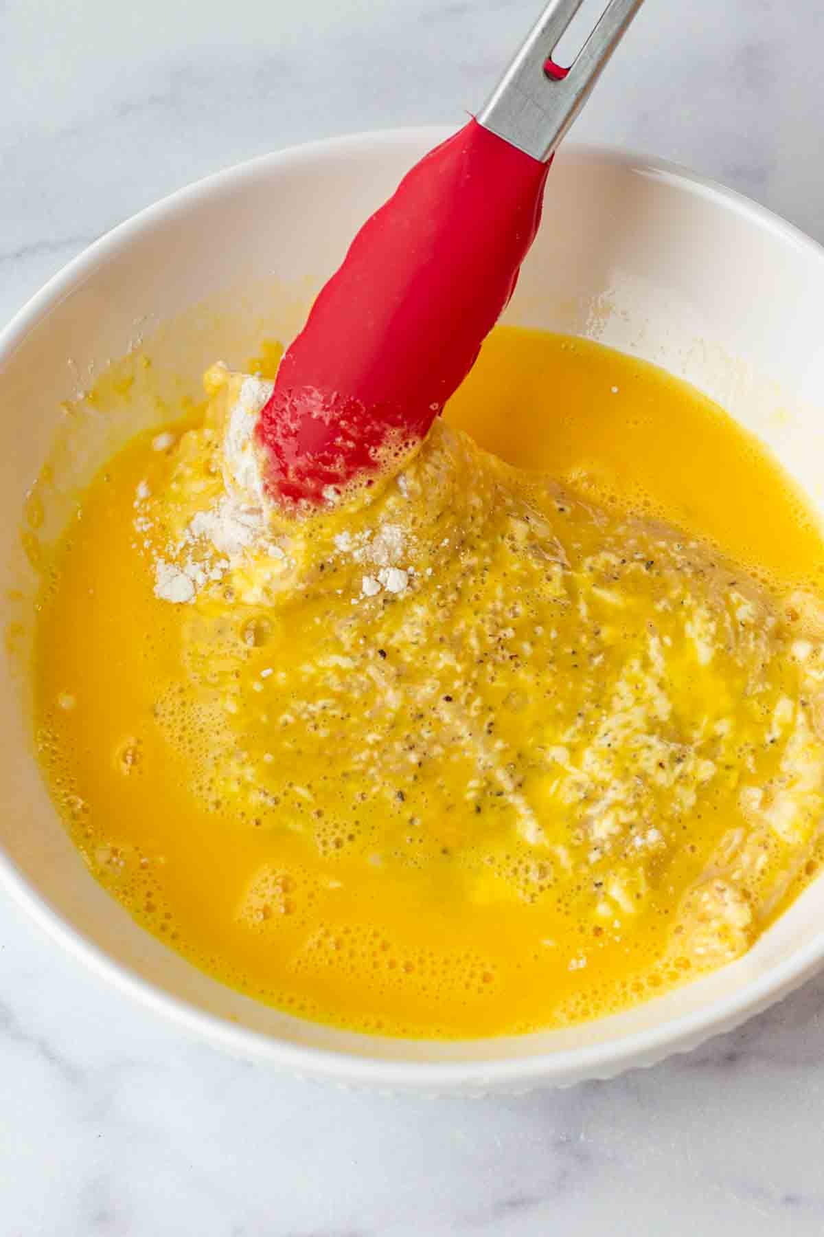 dipping chicken cutlet into beaten egg in a bowl