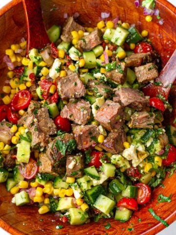 tossing chopped steak salad with vegetables in a wooden salad bowl