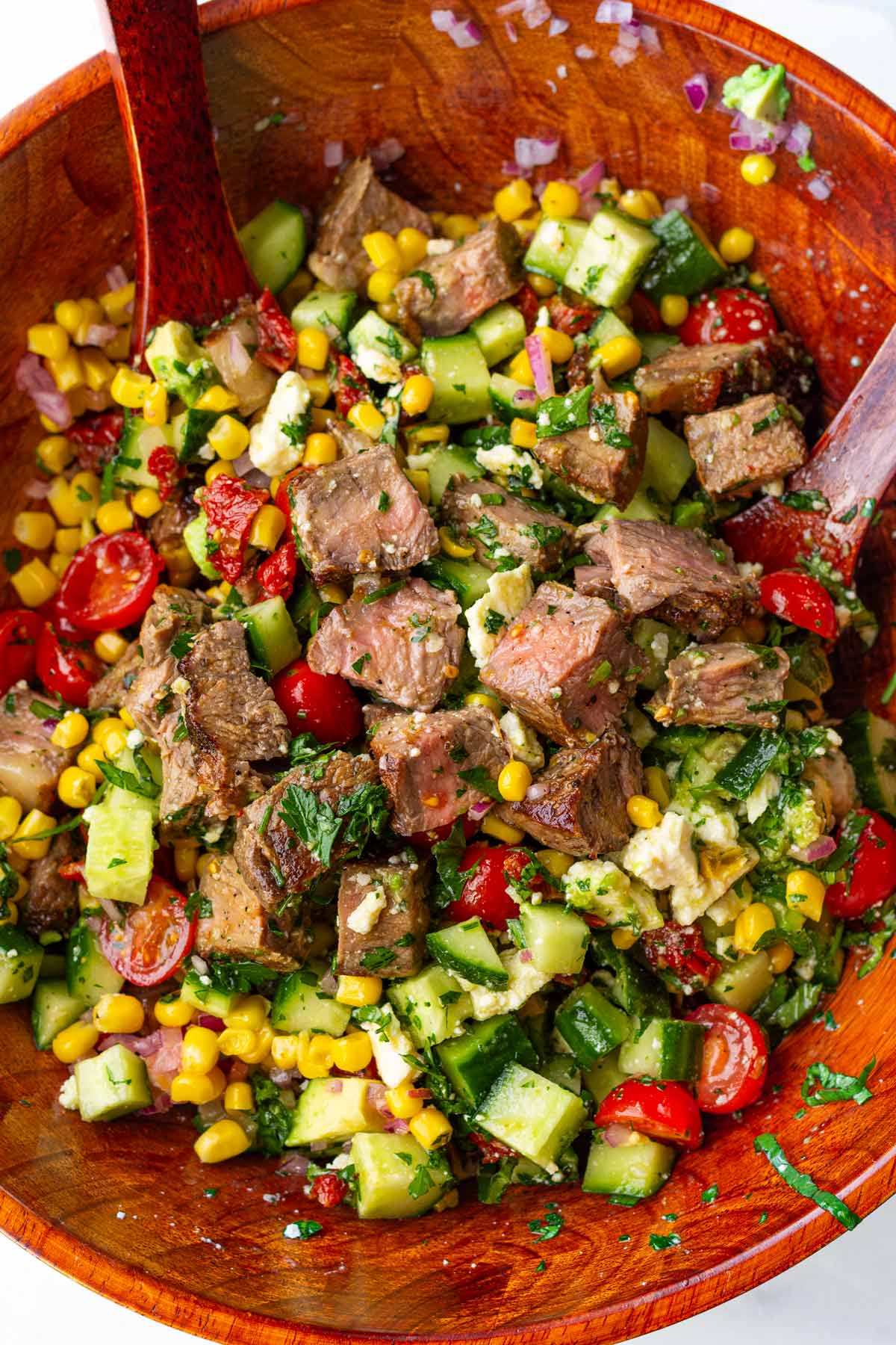 tossing chopped steak salad with vegetables in a wooden salad bowl