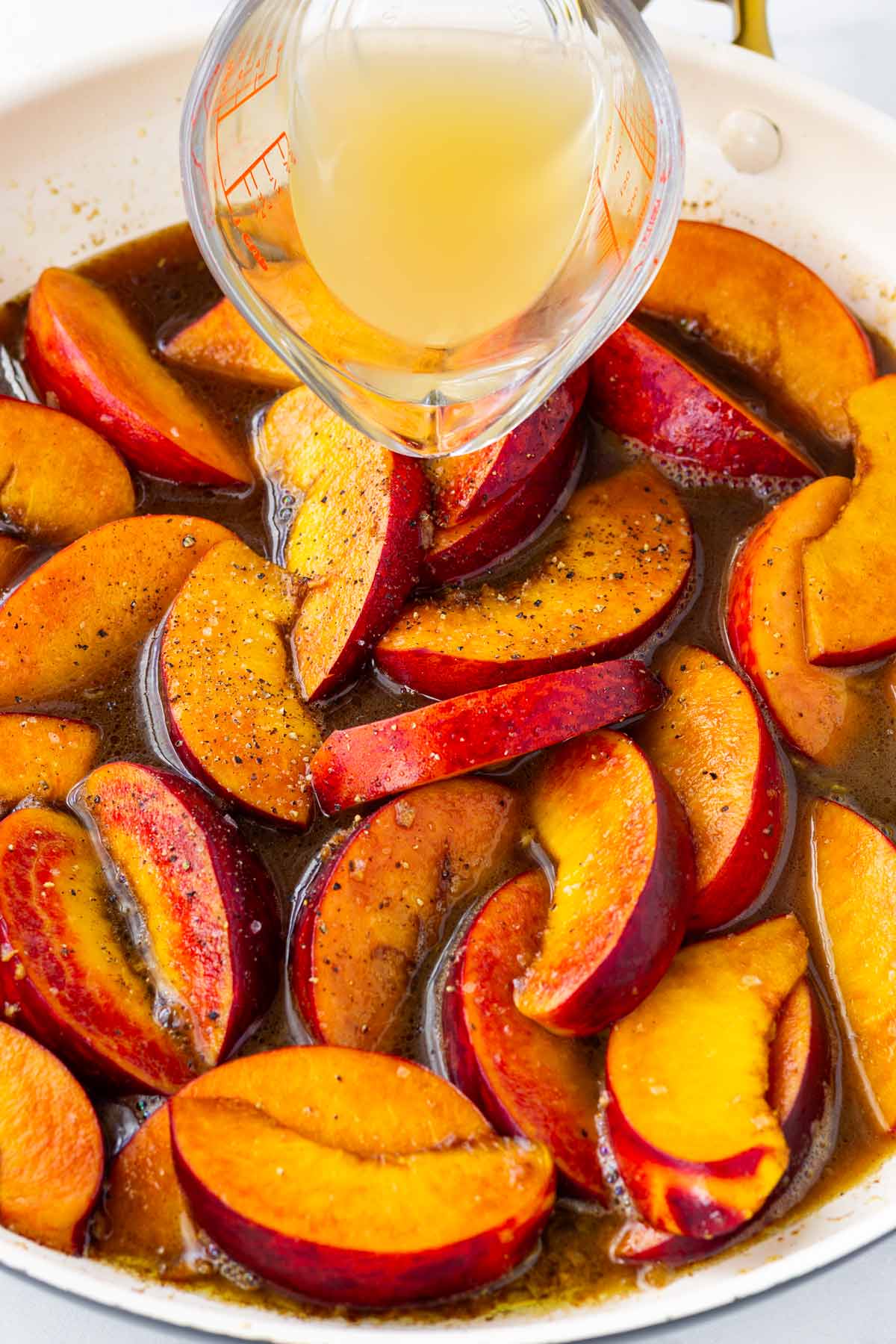 adding broth to the caramelized peaches in pan