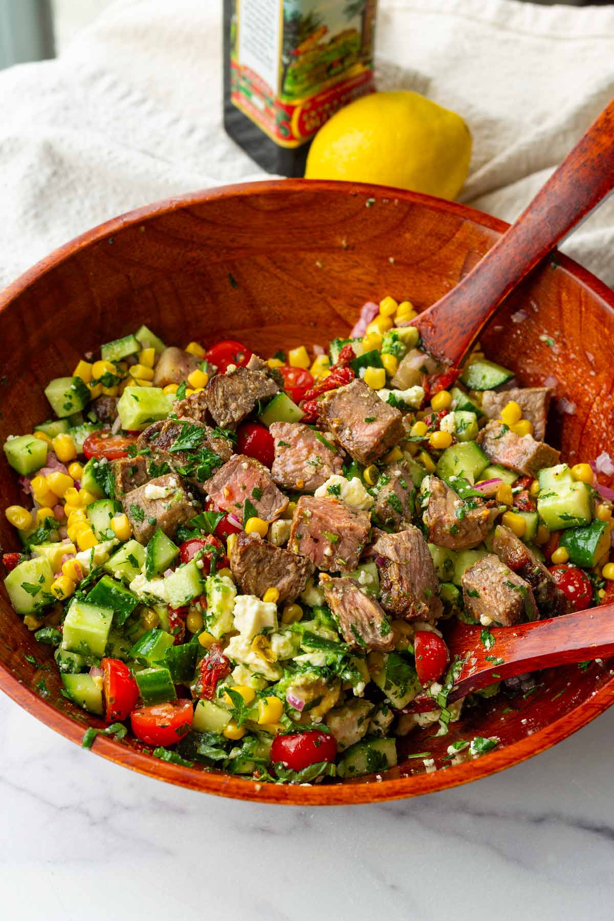 steak salad in wooden bowl with olive oil and lemon in the back