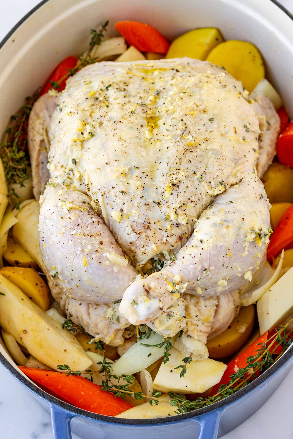 seasoned uncooked chicken resting on top of vegetables in the dutch oven