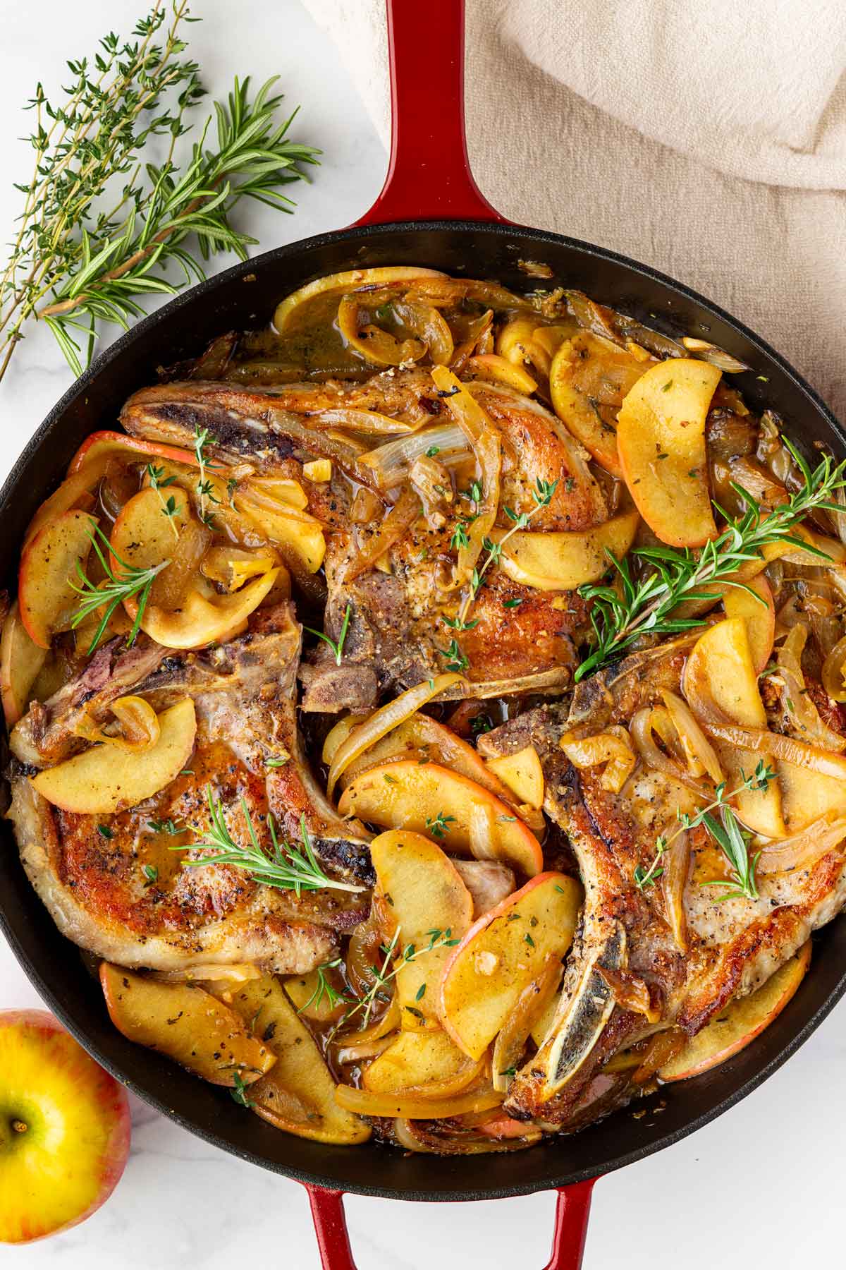 pork chops with apples and onions cooked in a red cast iron skillet