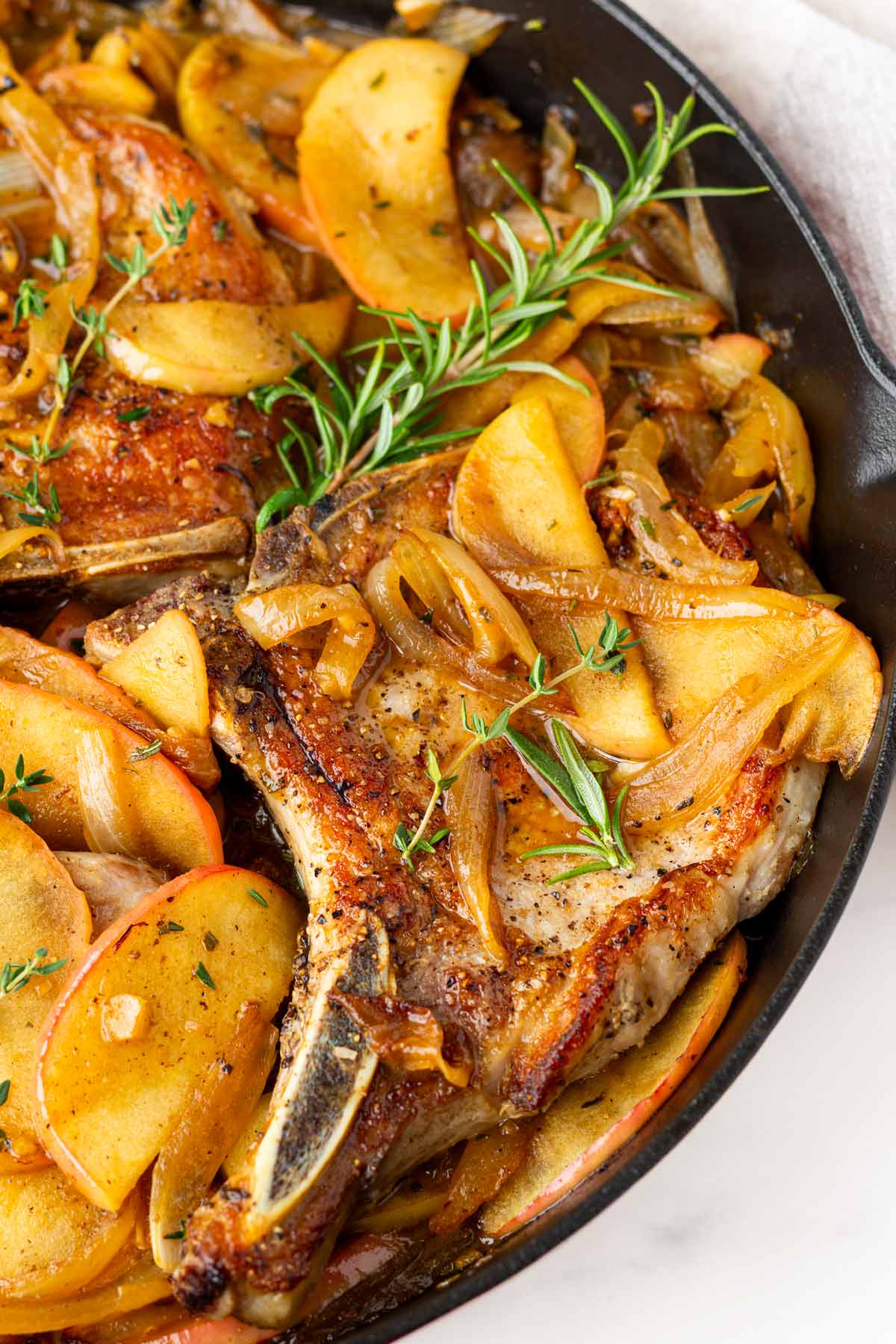 close up of a seared pork chop with apples, onions, and herbs