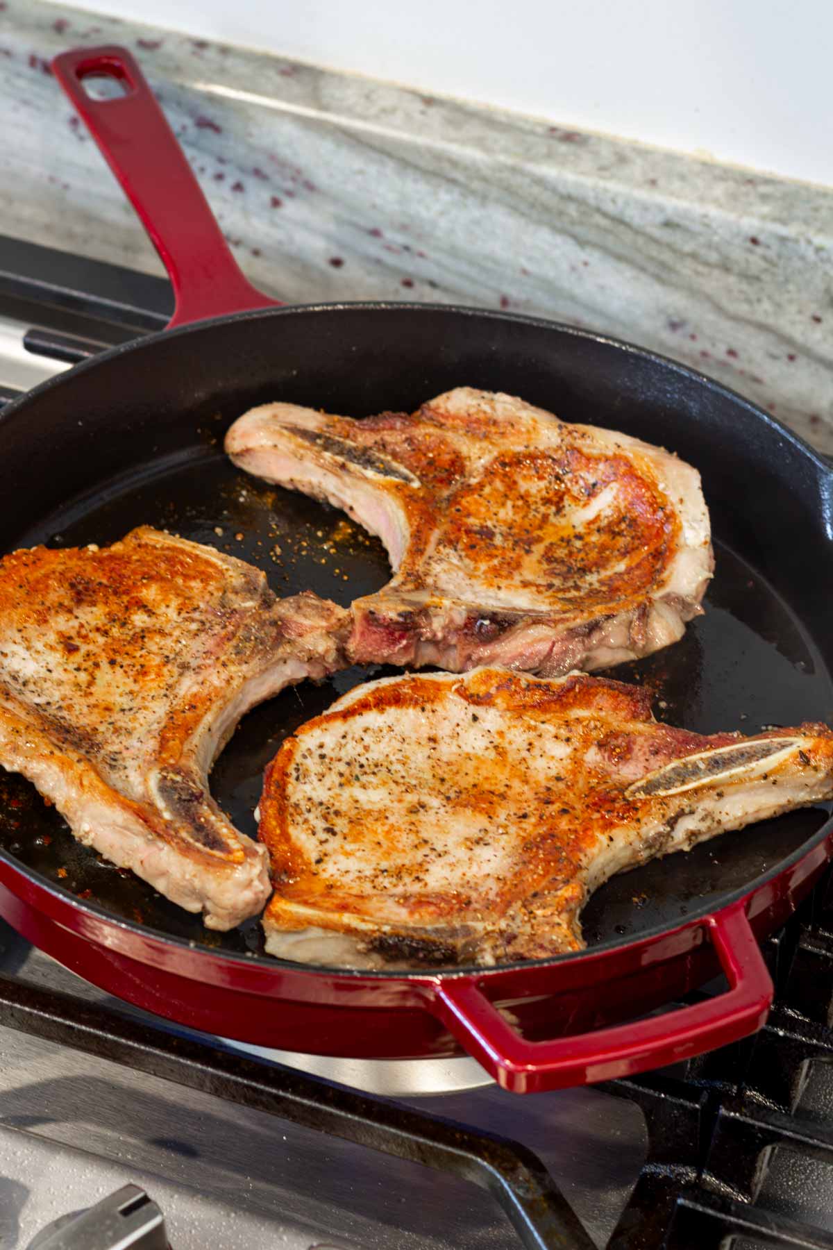 cooking pork chops in a red cast iron skillet