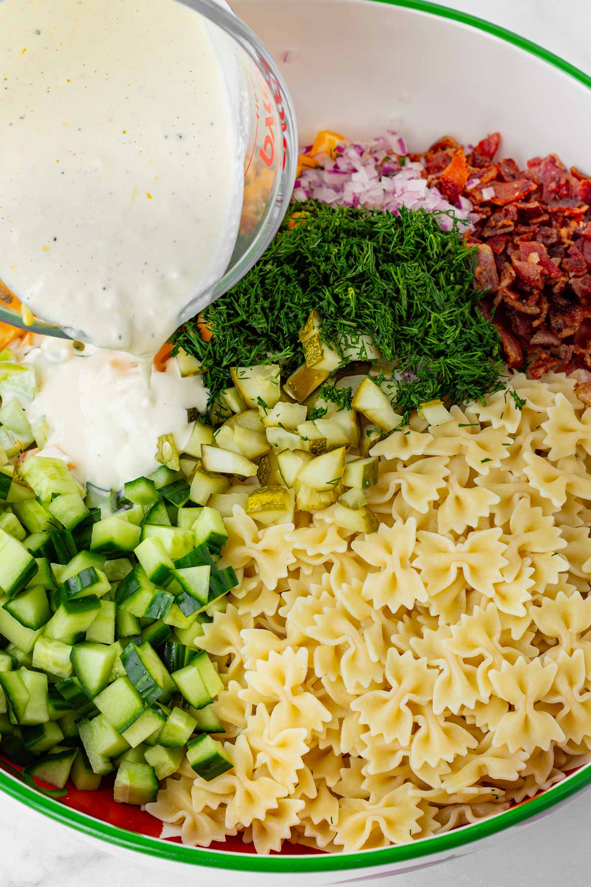 adding dressing into the dill pickle pasta salad
