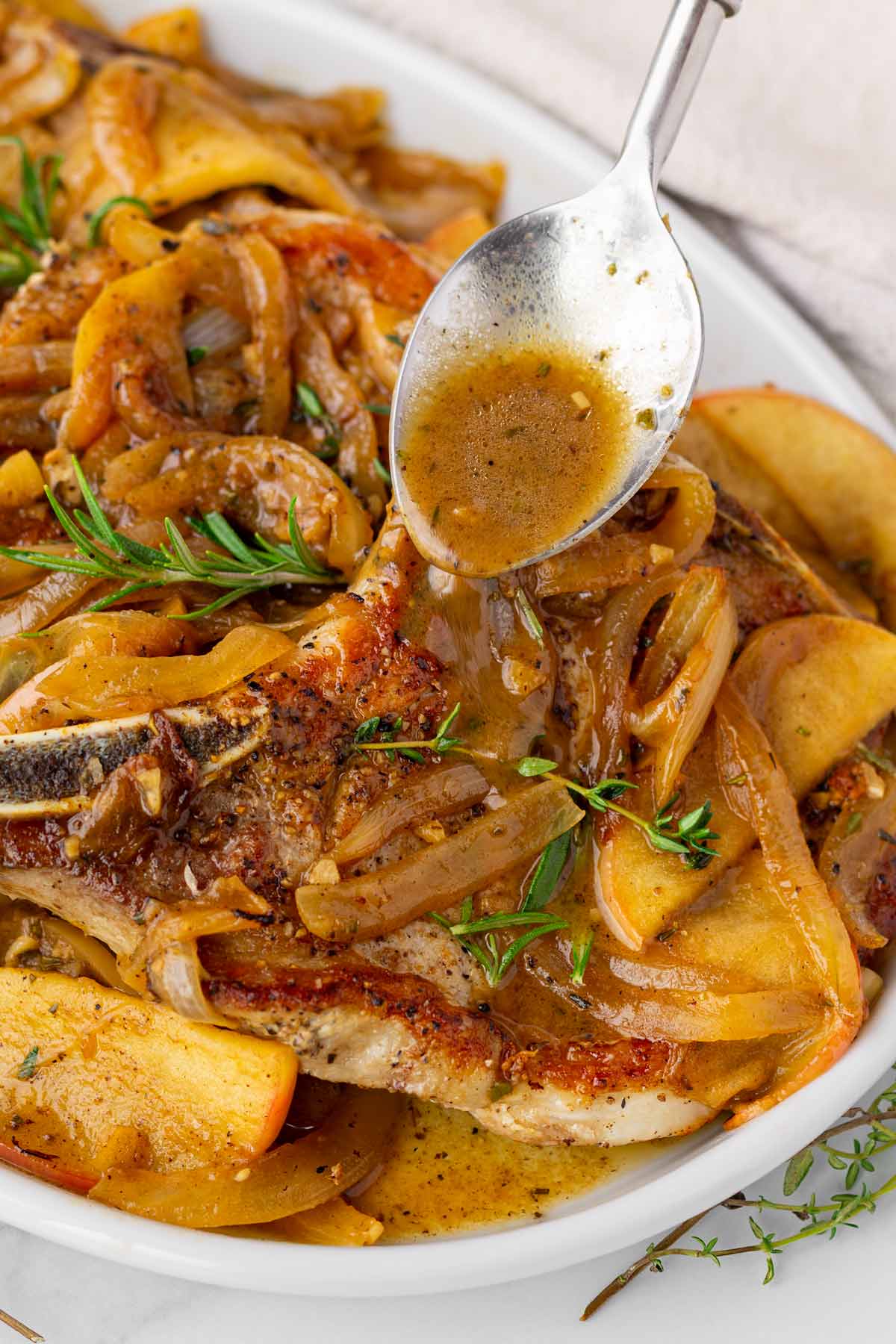 spooning the apple cider pan sauce over pork on a platter