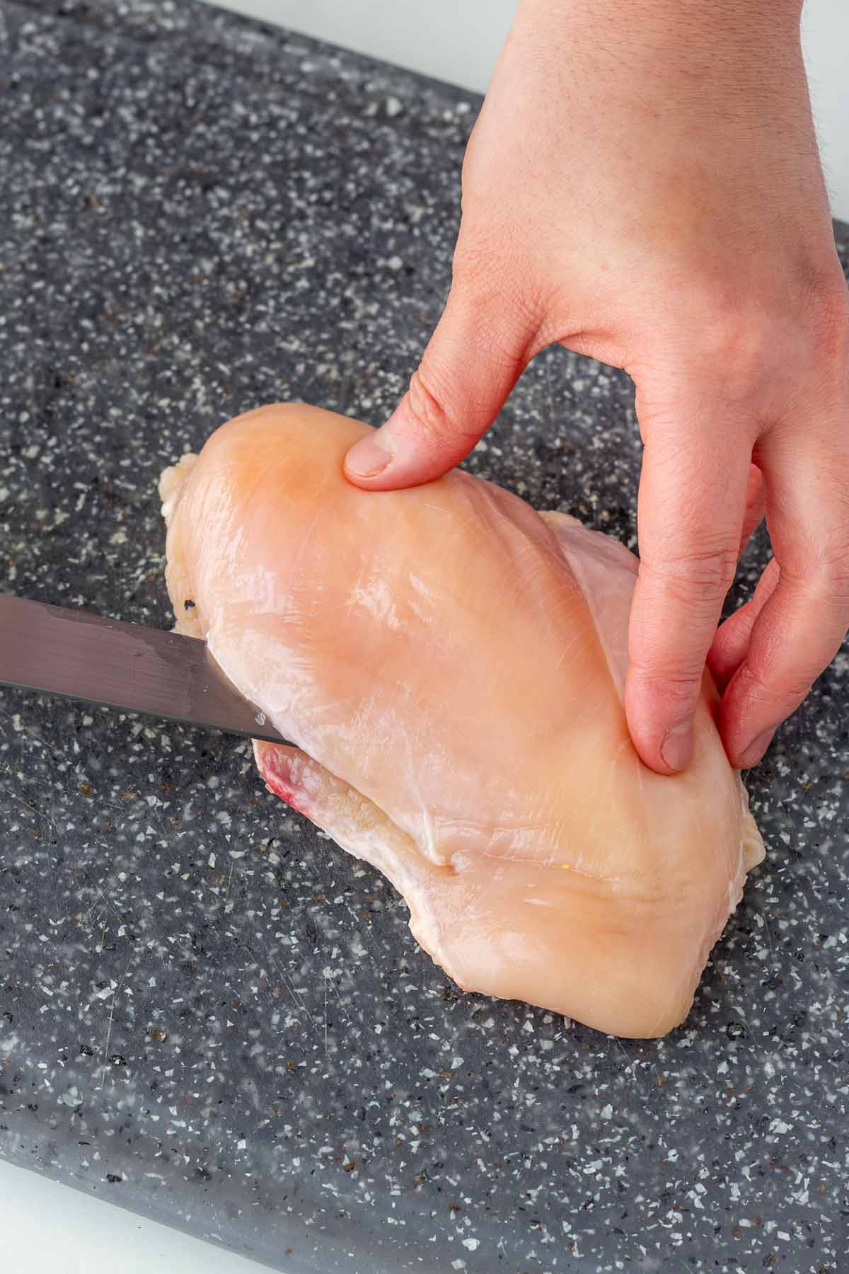 slicing open chicken breast on cutting board