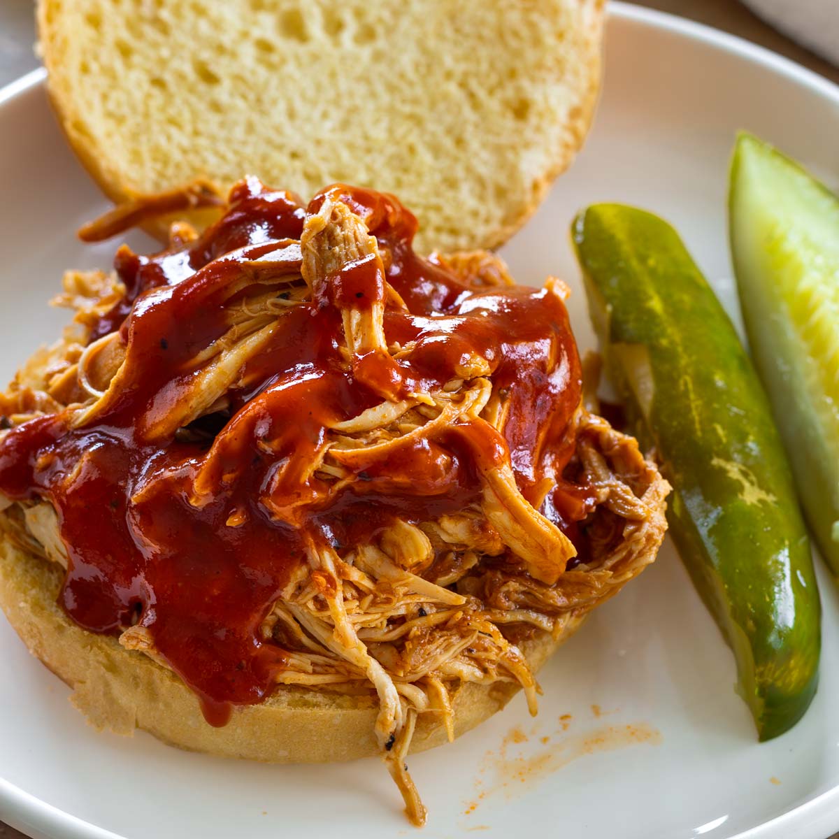 a pulled chicken sandwich with BBQ sauce and a side of pickles