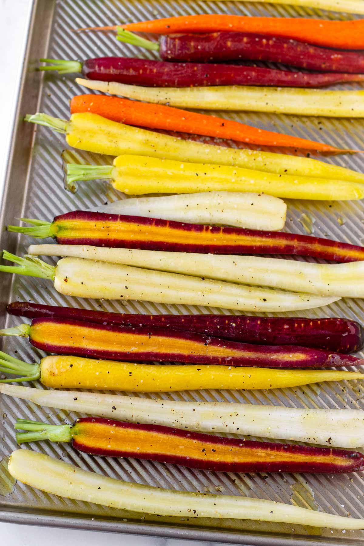 seasoned rainbow carrots on sheet pan before cooking