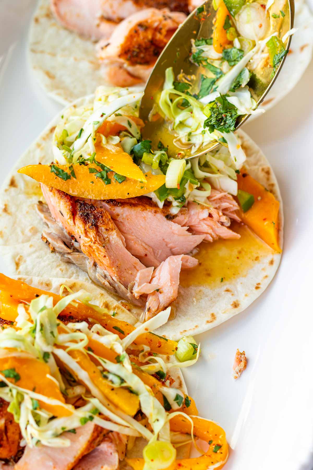 adding mango slaw topping to salmon tacos assembled