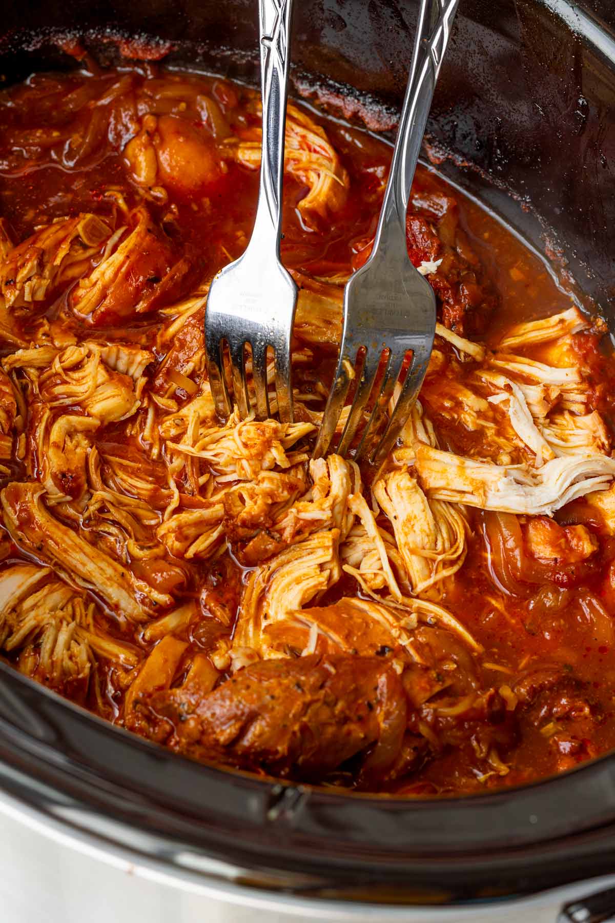 shredding chicken with two forks after the slow cooker pulled chicken is cooked