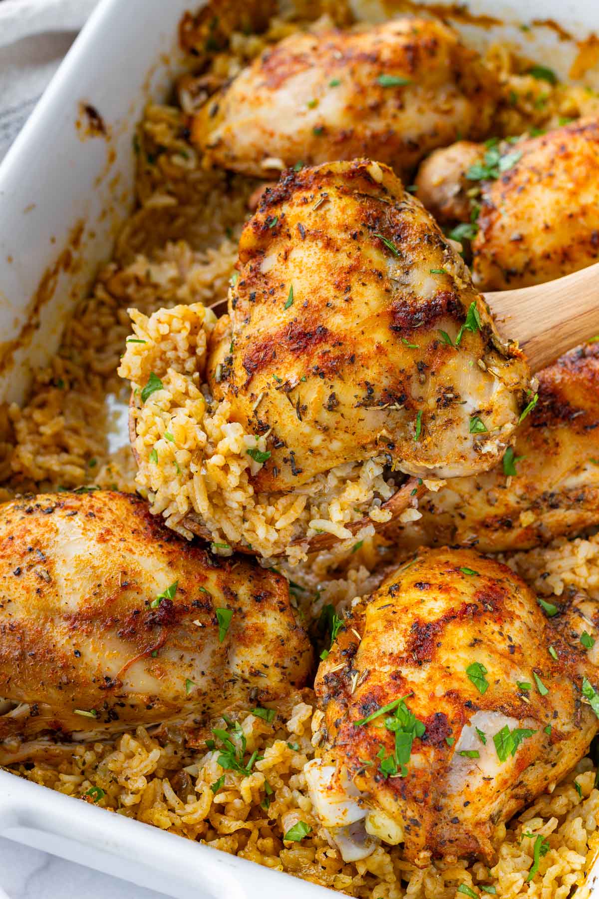 spooning baked chicken and rice serving with a wooden spoon