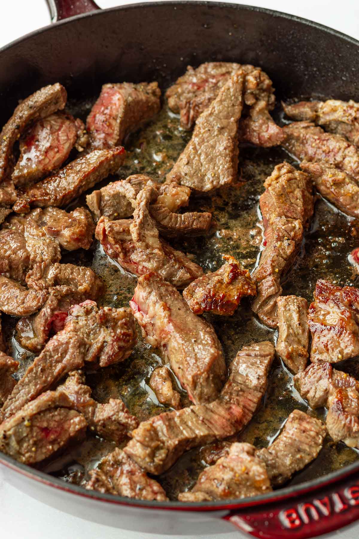 searing sliced beef sirloin in a cast iron pan