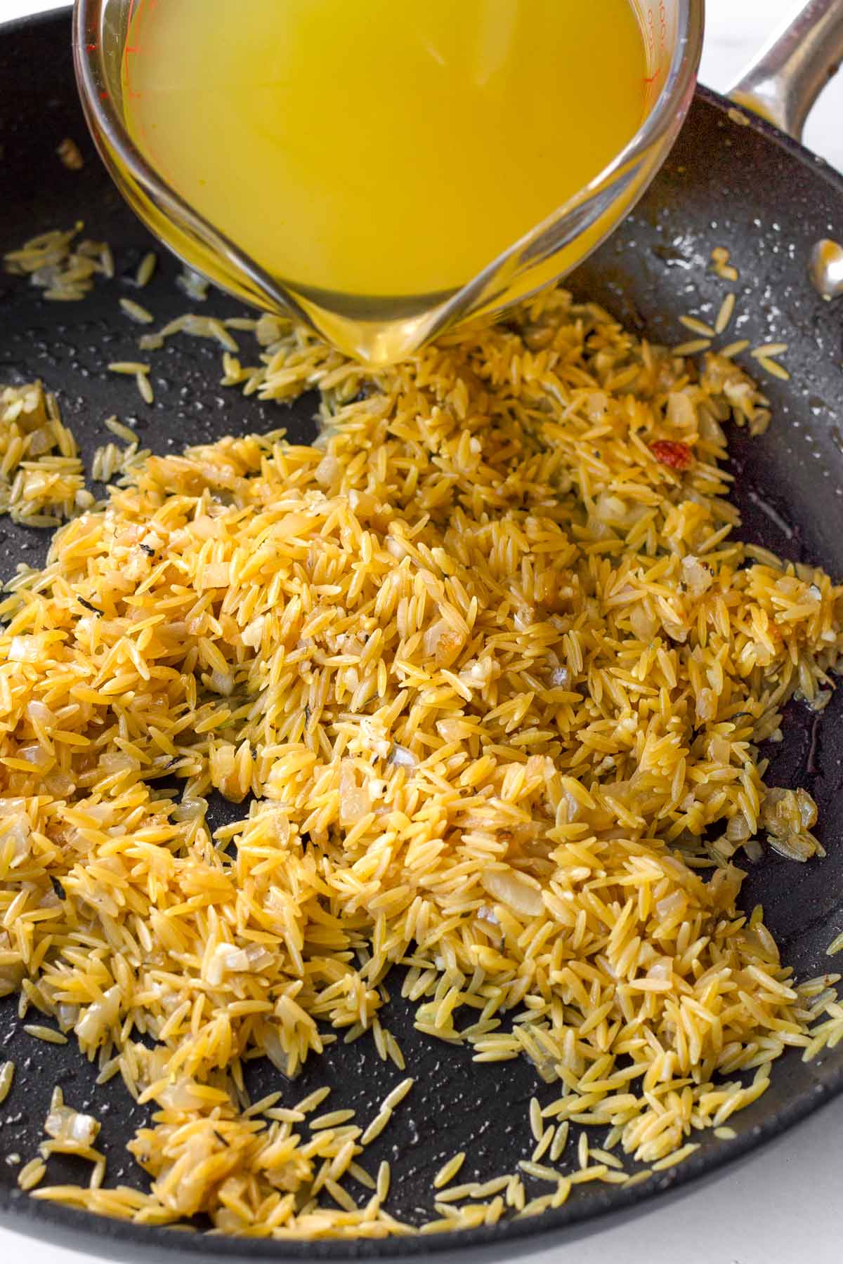 adding chicken broth to the orzo