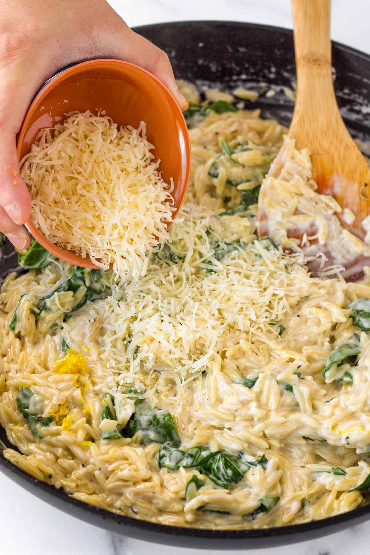 adding parmesan cheese to the creamy orzo